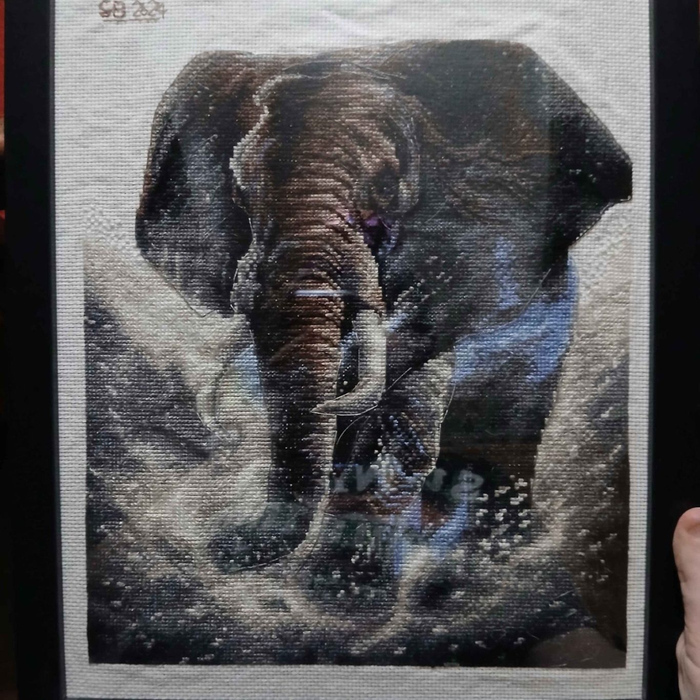 A detailed cross stitch of an elephant splashing in a watery landscape.